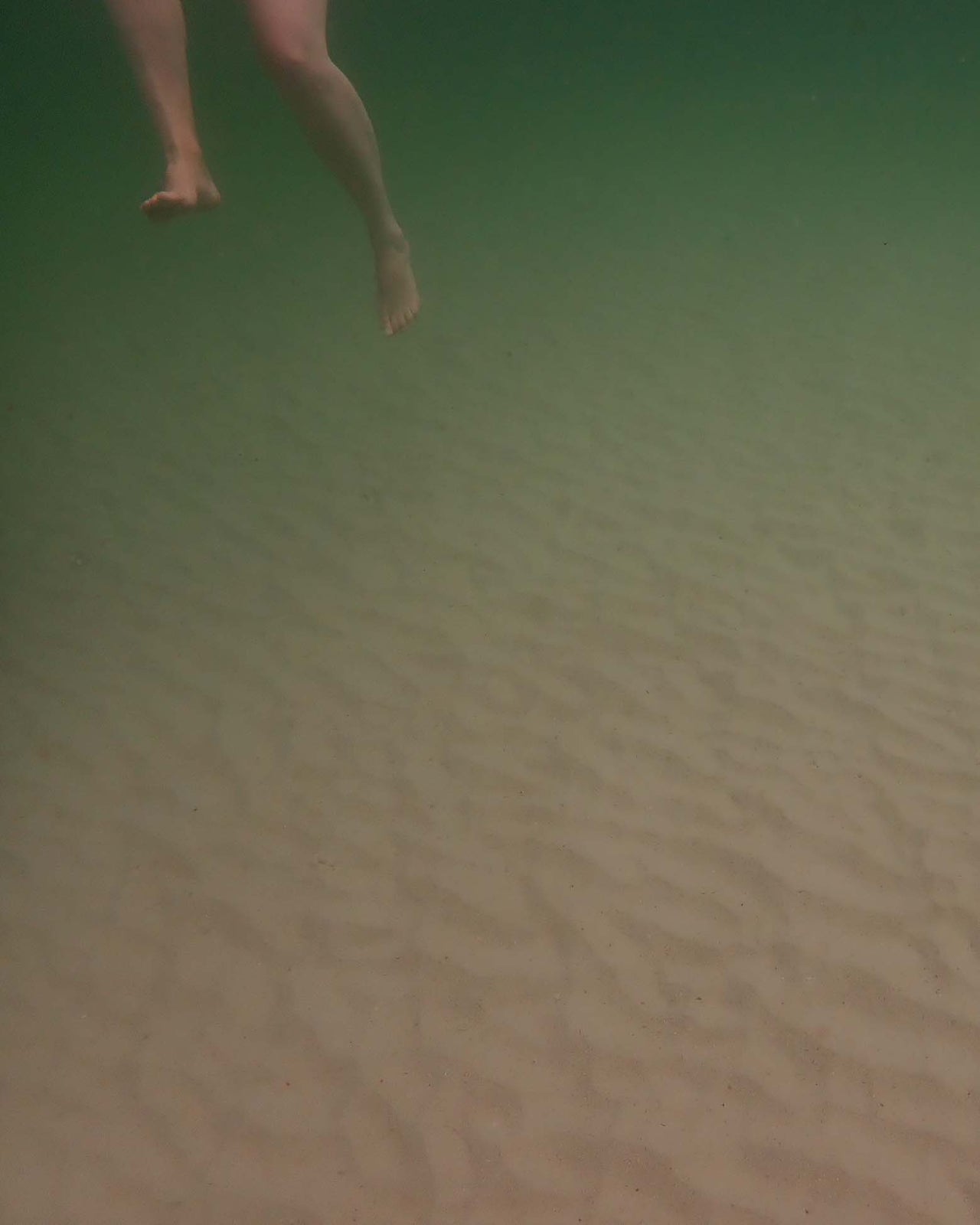 Photographer - Keri Muller:  An image taken undnerwater of a set of feet suspended above the sandy ocean floor.
